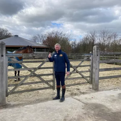 Ein Pferd auf einem Reitplatz, der durch ein doppeltes Holztor, das mit einem viersprossigen Holzzaun verbunden ist, umschlossen ist.